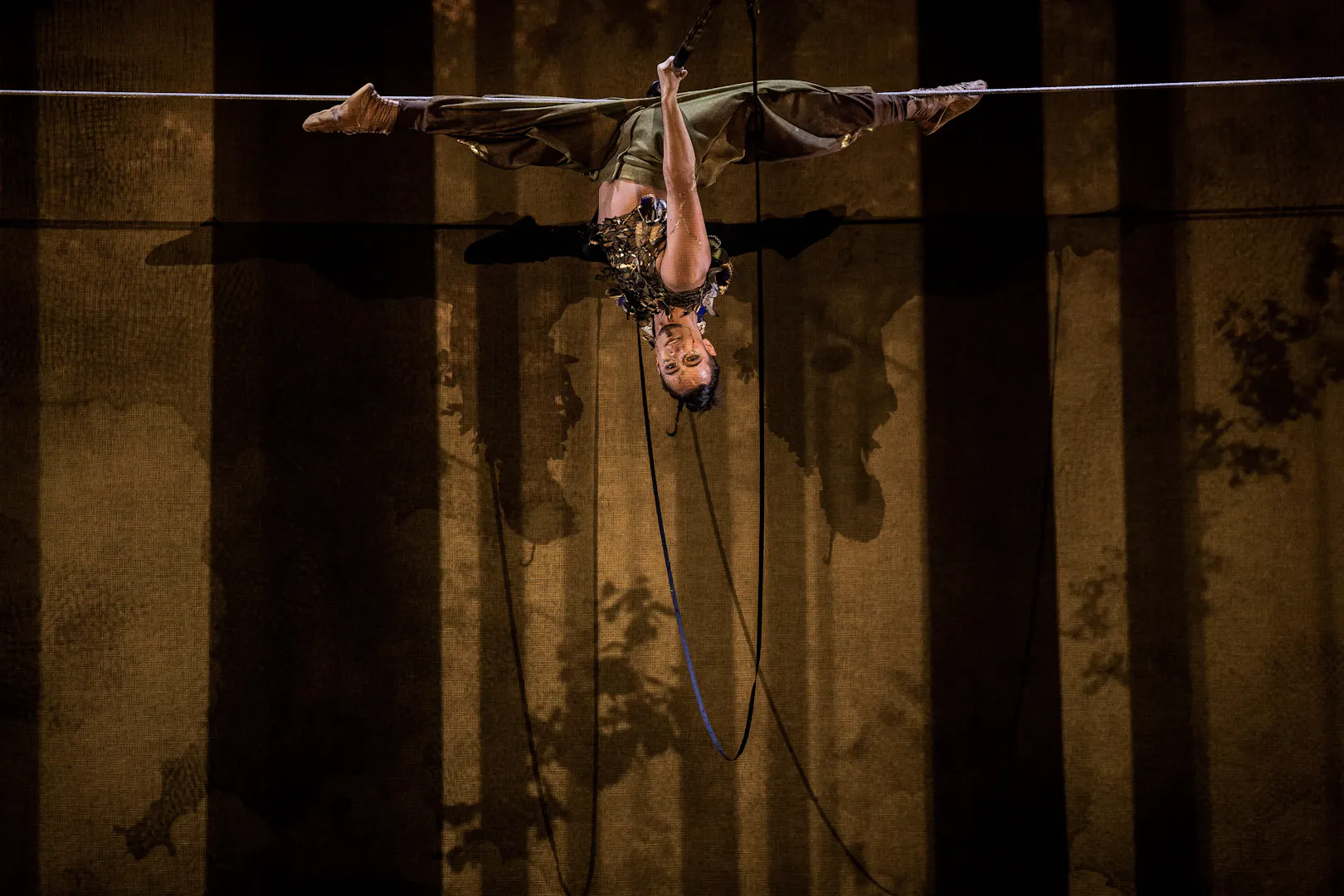 Performer suspended upside down during Cirque du Soleil Alizé stage show.
