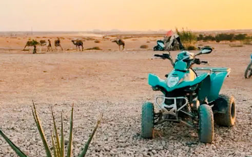 Quad bike parked on rocky terrain with camels in the background, Agafay Dunes, Marrakesh.