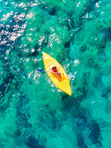 Aerial view of a person kayaking on clear ocean water.