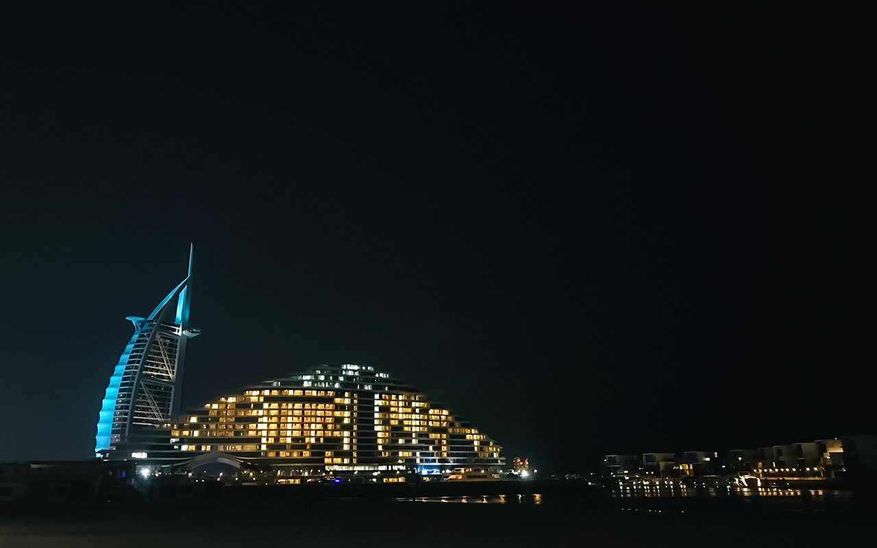 Palm Jumeirah beach at night with illuminated hotel and skyline.