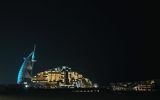 Palm Jumeirah beach at night with illuminated hotel and skyline.