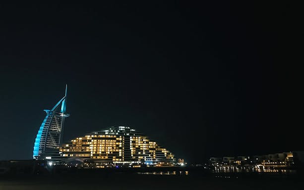 Palm Jumeirah beach at night with illuminated hotel and skyline.