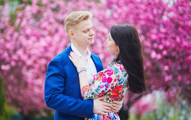 Couple embracing in front of blooming pink cherry blossoms during a romantic photoshoot.