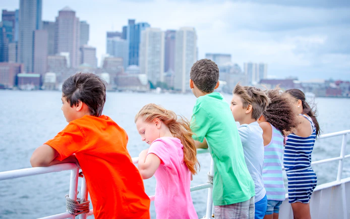 Children on a ferry from Boston to Spectacle Island, with city skyline in the background.