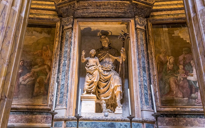 Statue inside the Roman Pantheon depicting a religious figure with a child, surrounded by frescoes.