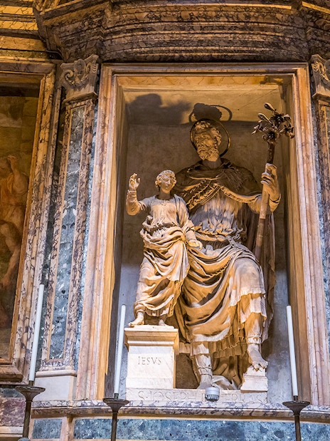 Statue inside the Roman Pantheon depicting a religious figure with a child, surrounded by frescoes.