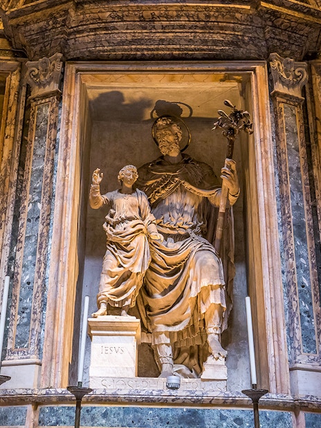 Statue inside the Roman Pantheon depicting a religious figure with a child, surrounded by frescoes.