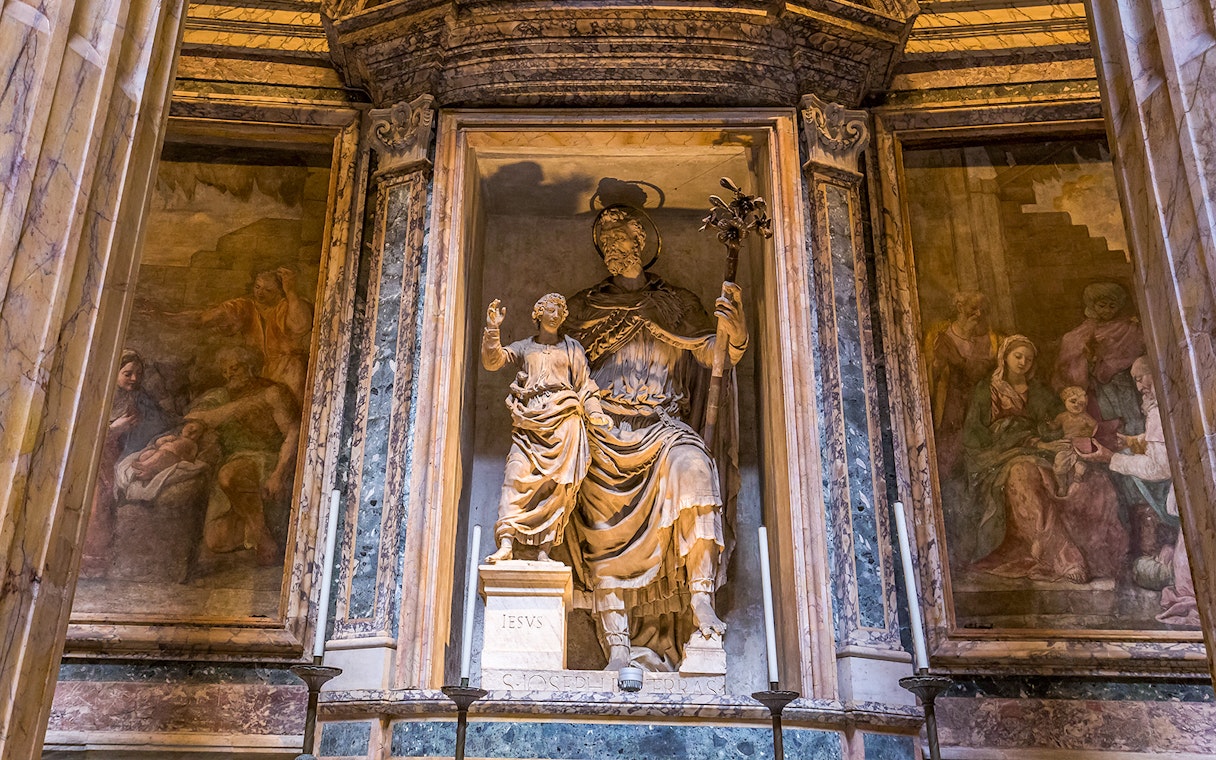 Statue inside the Roman Pantheon depicting a religious figure with a child, surrounded by frescoes.