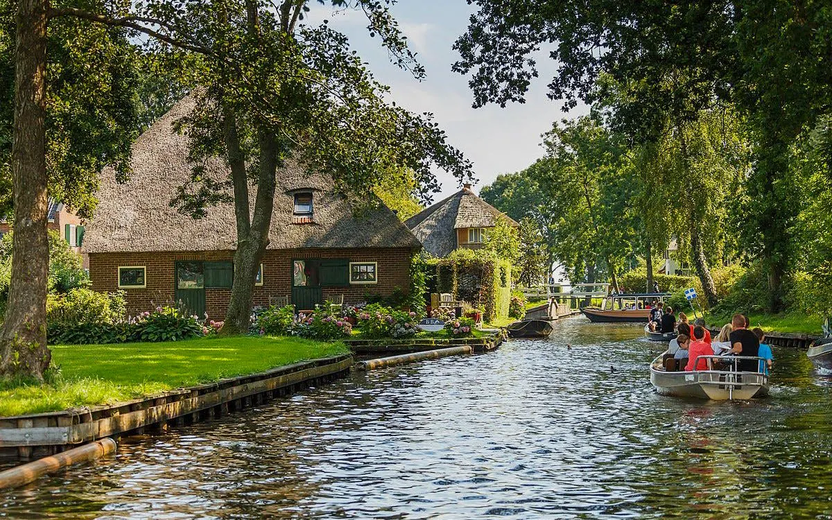 Boats navigating a canal in Giethoorn, passing traditional thatched-roof houses.