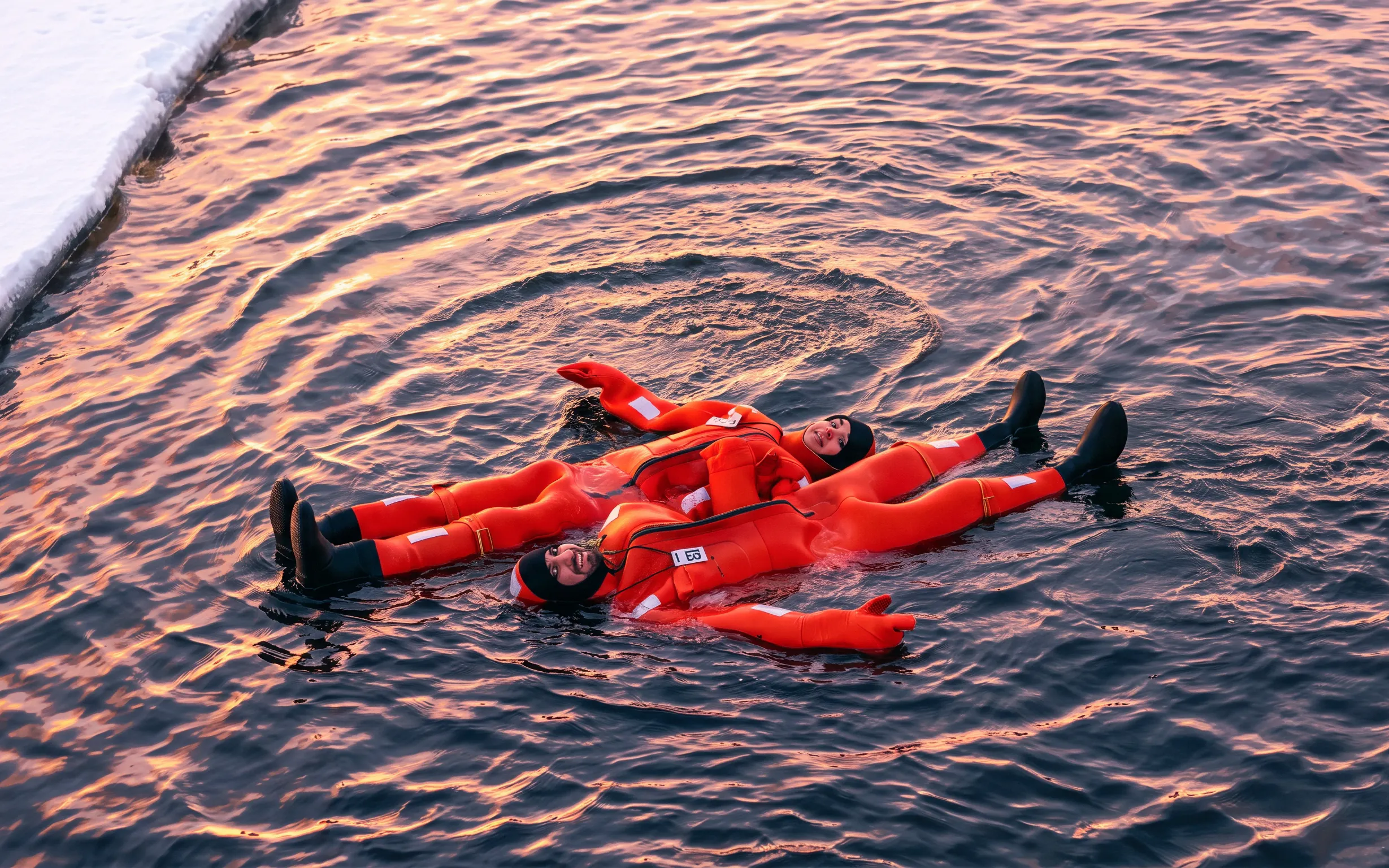 People in orange suits floating on icy water during an icebreaker cruise in Rovaniemi.