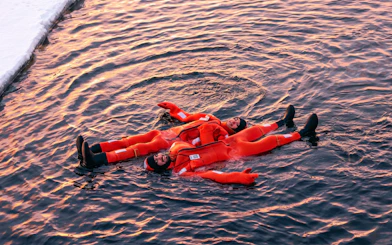 People in orange suits floating on icy water during an icebreaker cruise in Rovaniemi.