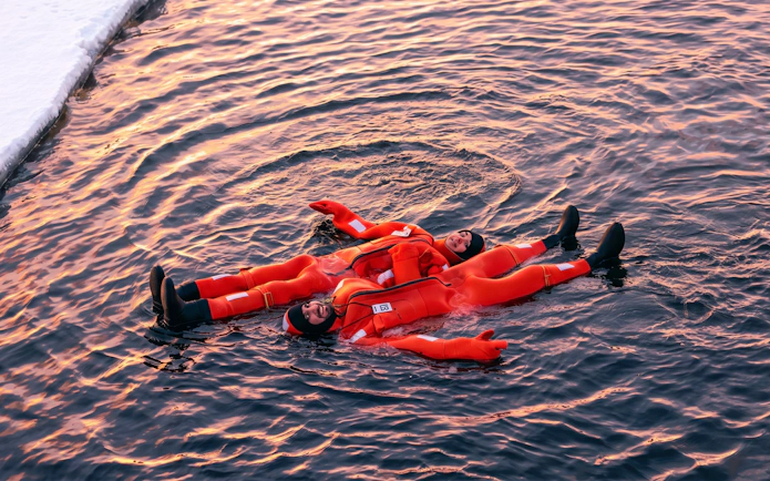 People in orange suits floating on icy water during an icebreaker cruise in Rovaniemi.