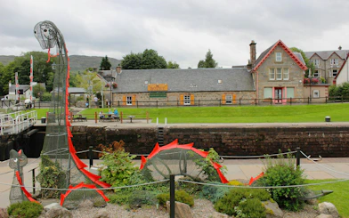 Loch Ness sculpture near canal and stone buildings in Scottish village.