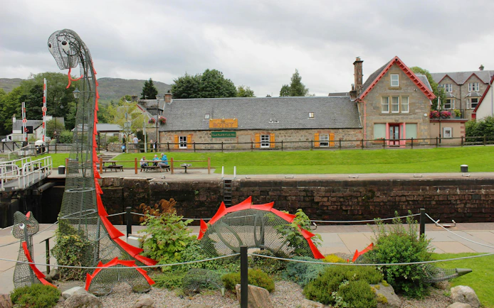 Loch Ness sculpture near canal and stone buildings in Scottish village.