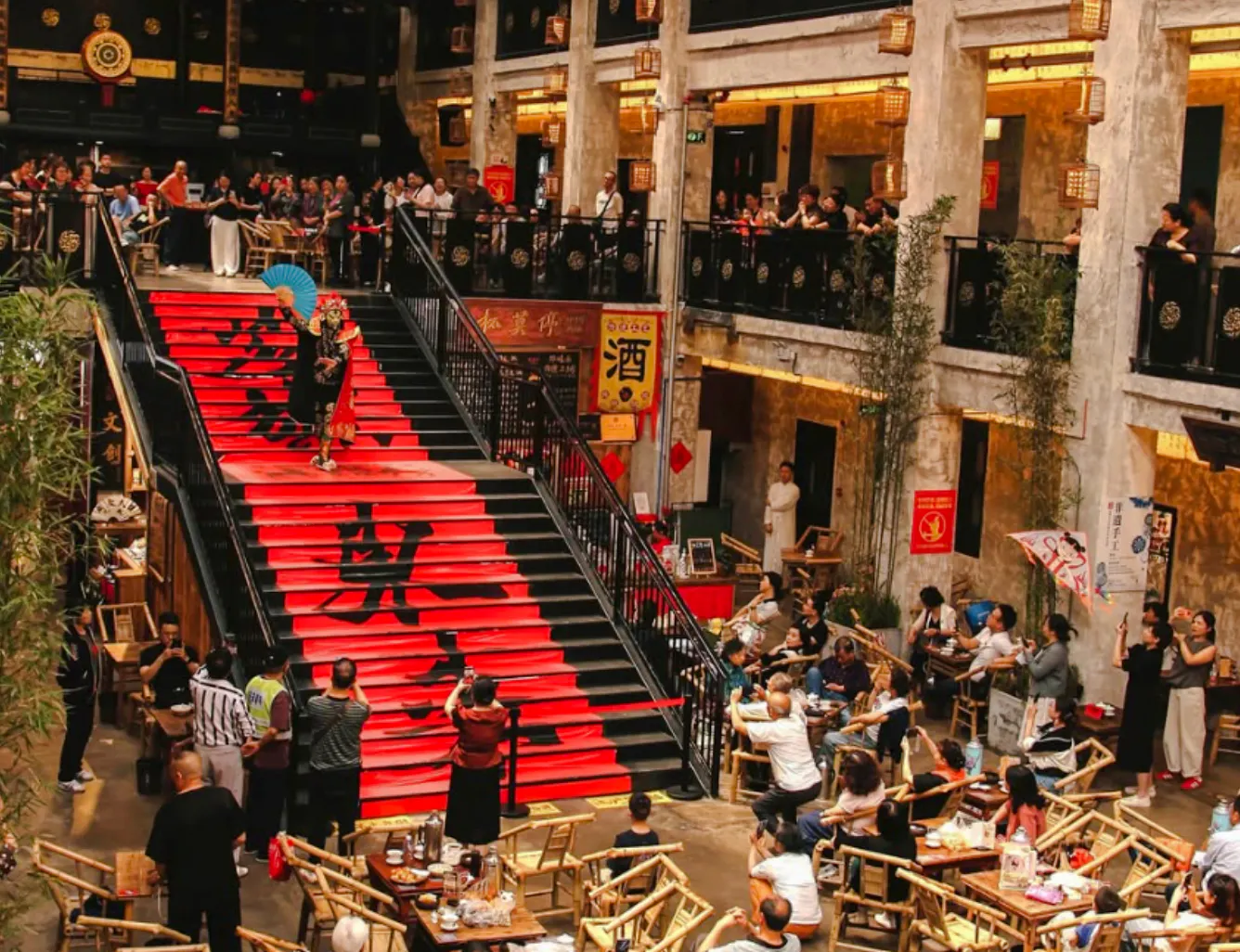 Chengdu Sichuan Opera performer on red staircase with audience in traditional theater setting.