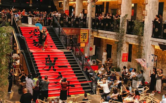 Chengdu Sichuan Opera performer on red staircase with audience in traditional theater setting.
