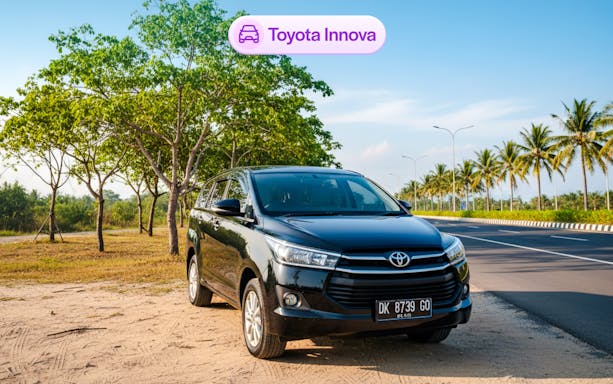 Toyota Innova parked on a scenic road in Bali with palm trees and clear sky.