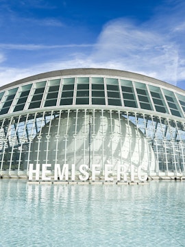 Hemisferic building with glass facade reflecting in water, Valencia, Spain.