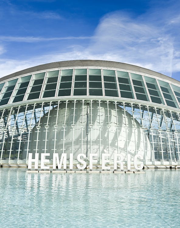 Hemisferic building with glass facade reflecting in water, Valencia, Spain.