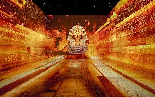 Tutankhamun mask projection in immersive exhibition with hieroglyphic walls.