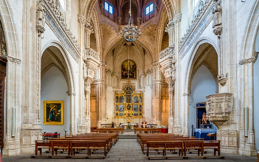 Interior of the Monastery of San Juan de los Reyes, Toledo, Spain, featuring ornate arches and altar.