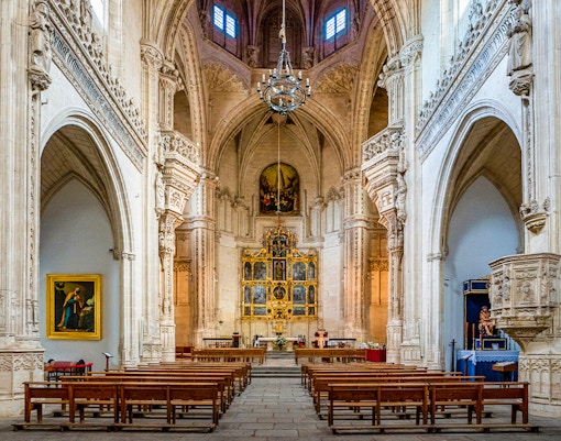 Interior of the Monastery of San Juan de los Reyes, Toledo, Spain, featuring ornate arches and altar.