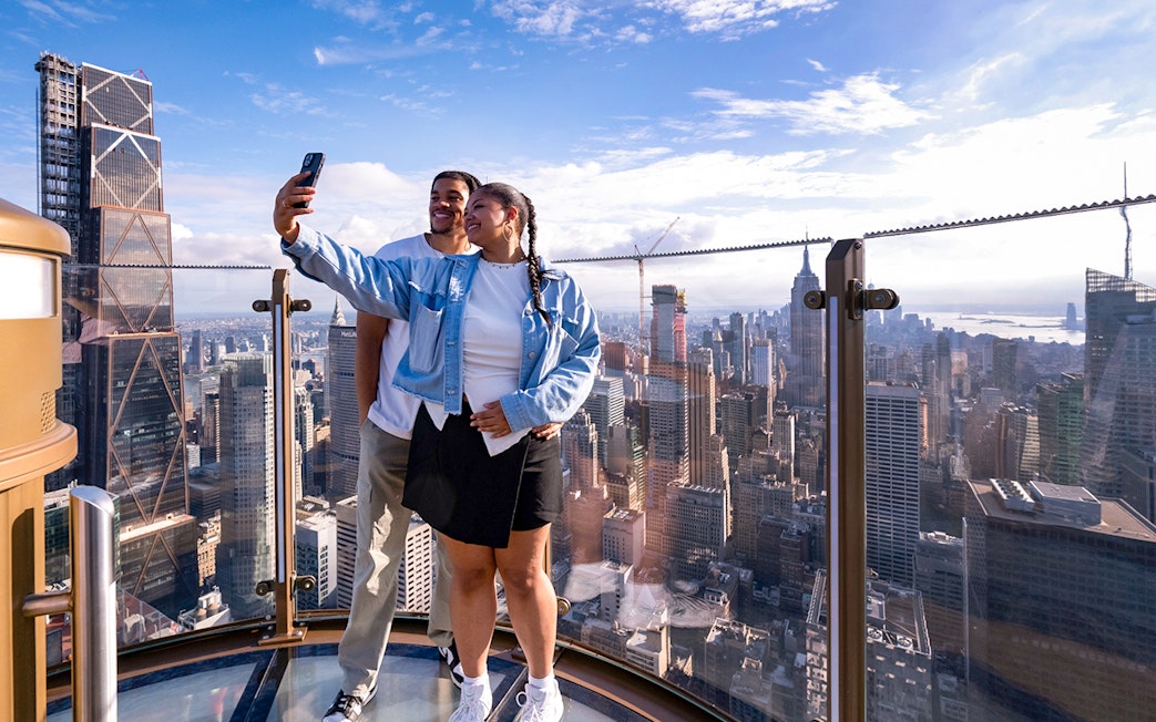 Couple taking a selfie at Top of the Rock Observation Deck with New York City skyline.