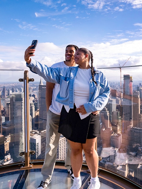 Couple taking a selfie at Top of the Rock Observation Deck with New York City skyline.