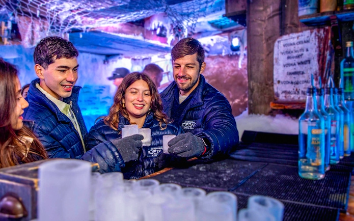Visitors enjoying drinks at Icebar Amsterdam, surrounded by ice sculptures and vibrant lighting.