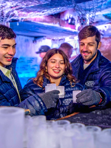 Visitors enjoying drinks at Icebar Amsterdam, surrounded by ice sculptures and vibrant lighting.