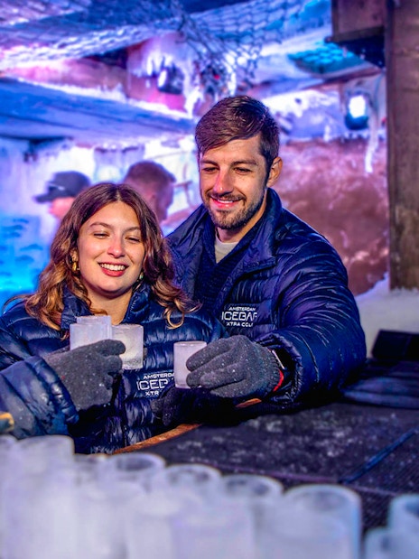 Visitors enjoying drinks at Icebar Amsterdam, surrounded by ice sculptures and vibrant lighting.
