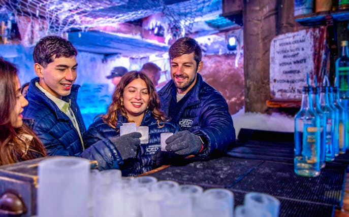 Visitors enjoying drinks at Icebar Amsterdam, surrounded by ice sculptures and vibrant lighting.