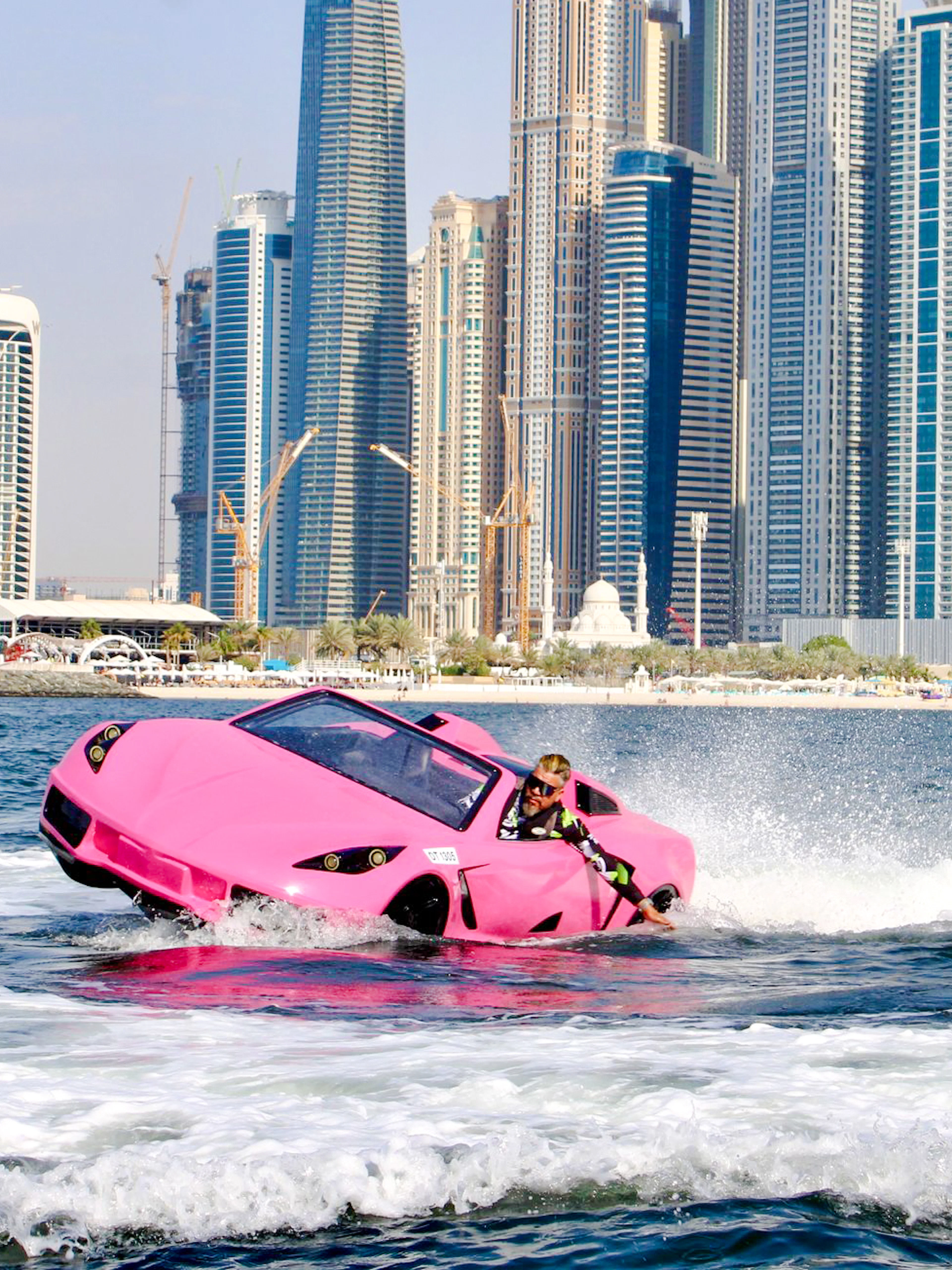 Man driving pink jet car on water with Dubai skyline in background.