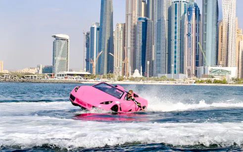 Man driving pink jet car on water with Dubai skyline in background.