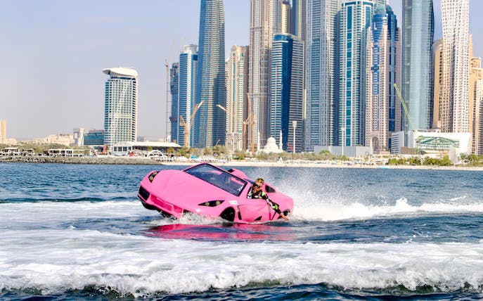 Man driving pink jet car on water with Dubai skyline in background.