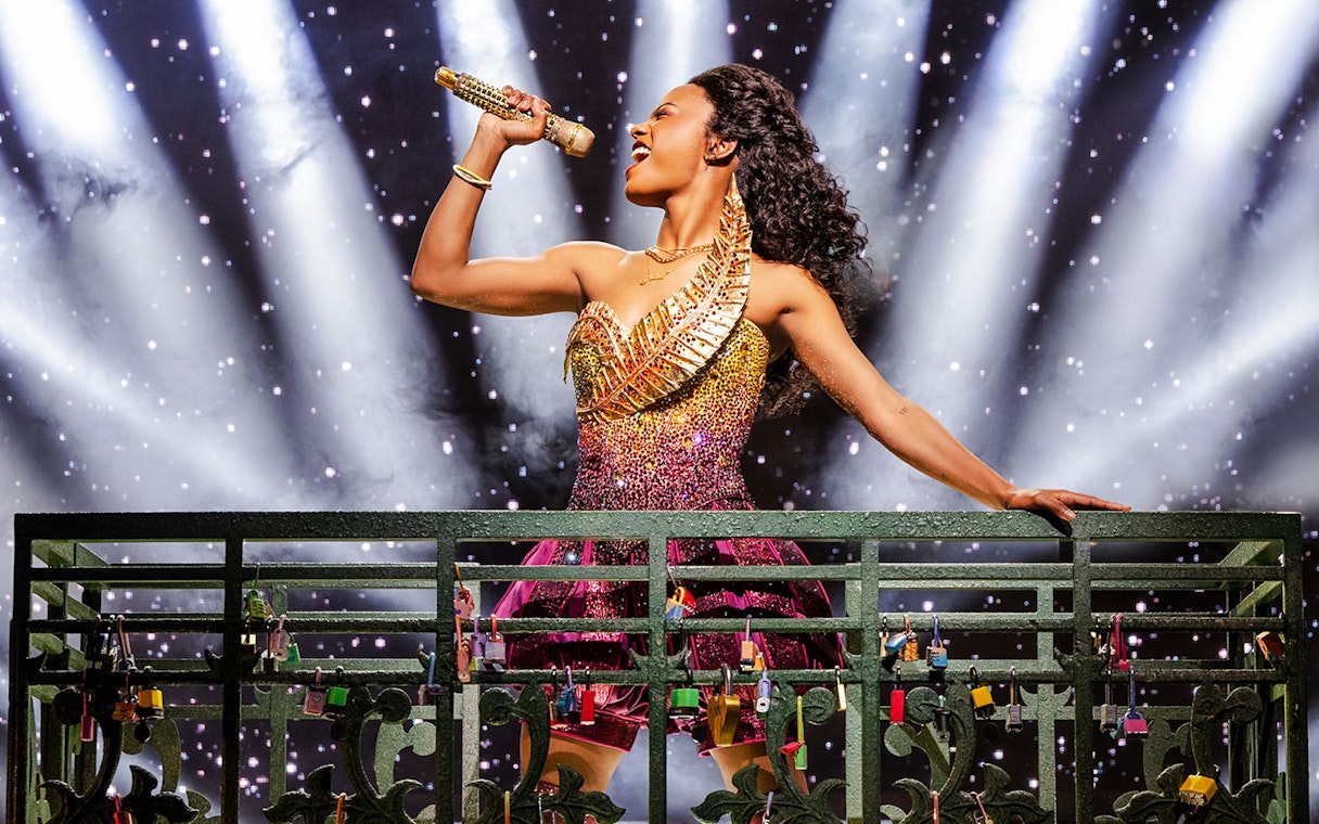 Performer singing on stage in & Juliet musical with spotlight background.