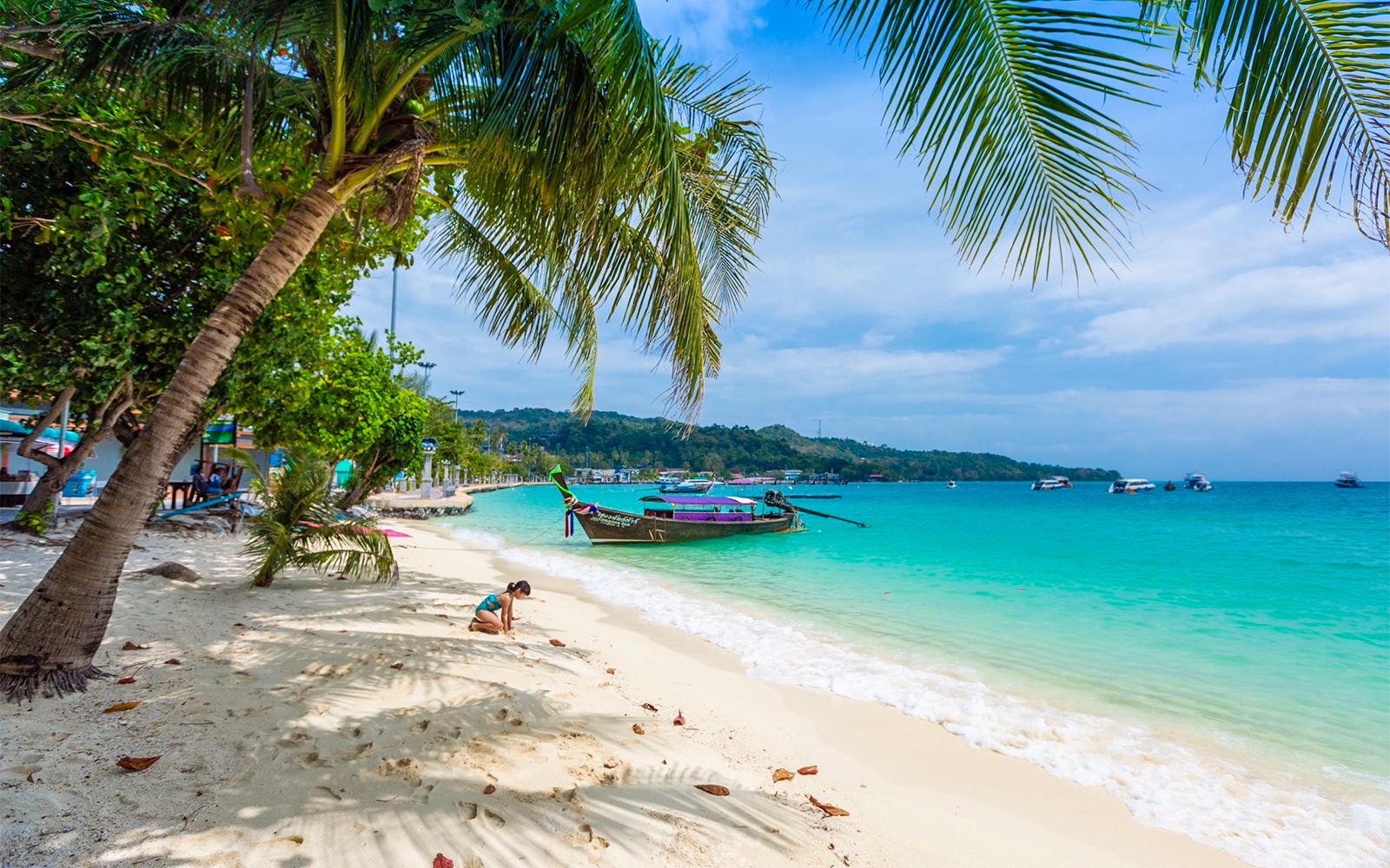 Person on sand beach near speedboat with turquoise water in Phi Phi, Thailand.