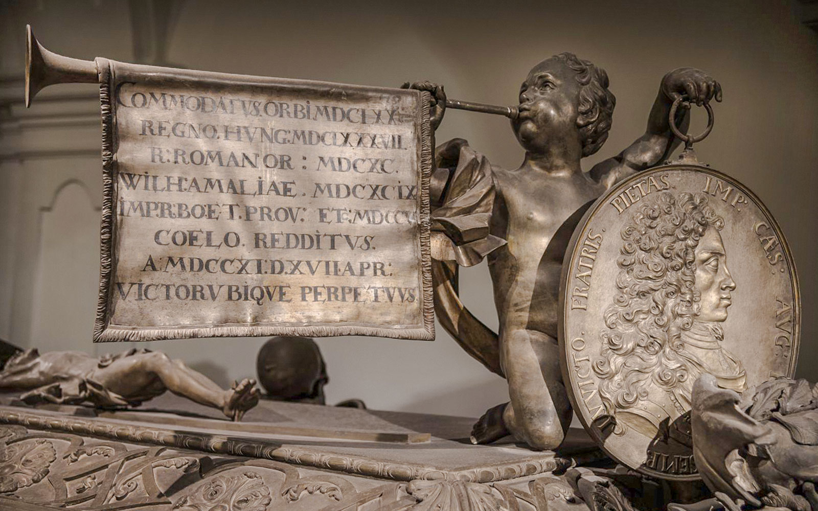 Sculpture detail inside Minoritenkirche, Vienna, featuring a cherub with a trumpet and inscribed banner.