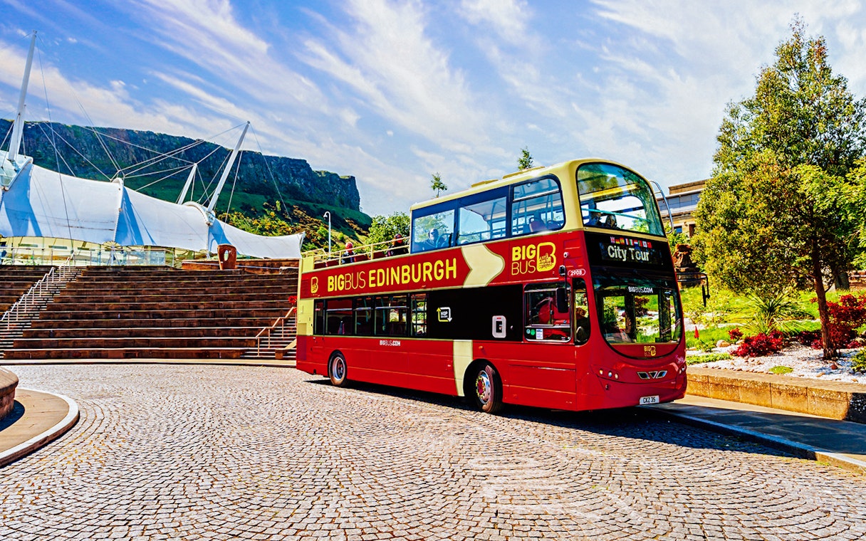 Edinburgh hop-on hop-off bus near modern architecture and Arthur's Seat.