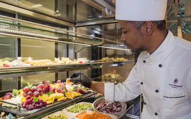 Chef arranging fresh fruit display at Rome Fiumicino Airport lounge.