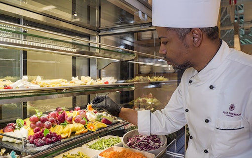 Chef arranging fresh fruit display at Rome Fiumicino Airport lounge.