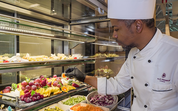 Chef arranging fresh fruit display at Rome Fiumicino Airport lounge.