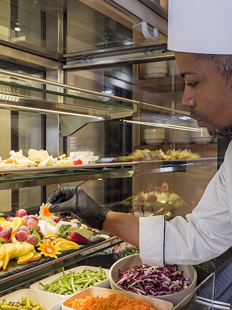 Chef arranging fresh fruit display at Rome Fiumicino Airport lounge.