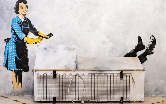 Street art of a woman pushing a man into a freezer at the Banksy Museum in Lisbon.