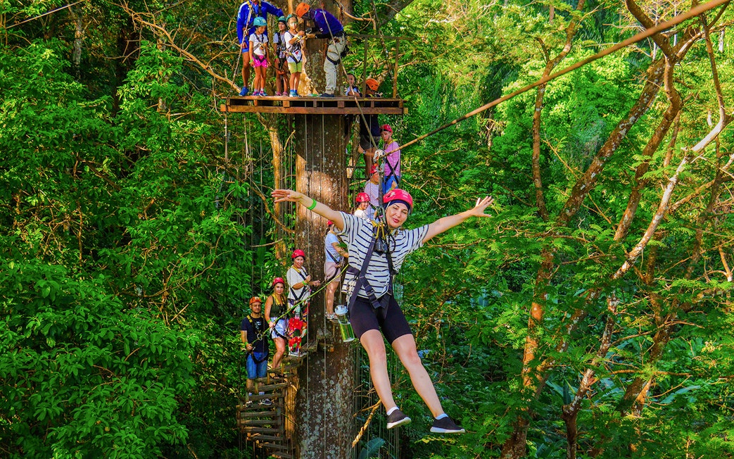 Tourist zip lining through lush forest at Hanuman World Zipline, Thailand.