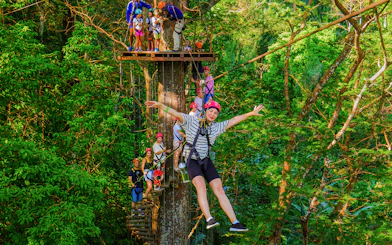 Tourist zip lining through lush forest at Hanuman World Zipline, Thailand.