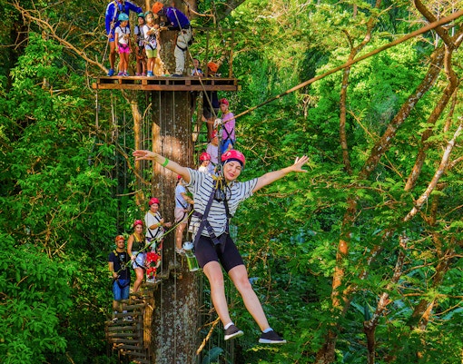 Tourist zip lining through lush forest at Hanuman World Zipline, Thailand.