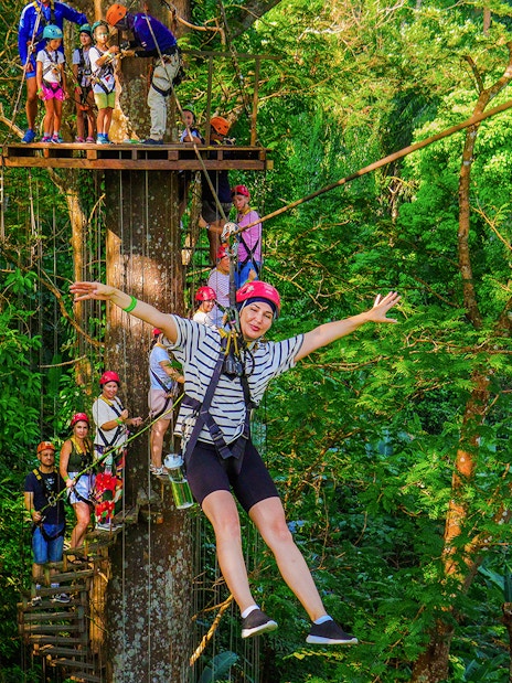 Tourist zip lining through lush forest at Hanuman World Zipline, Thailand.
