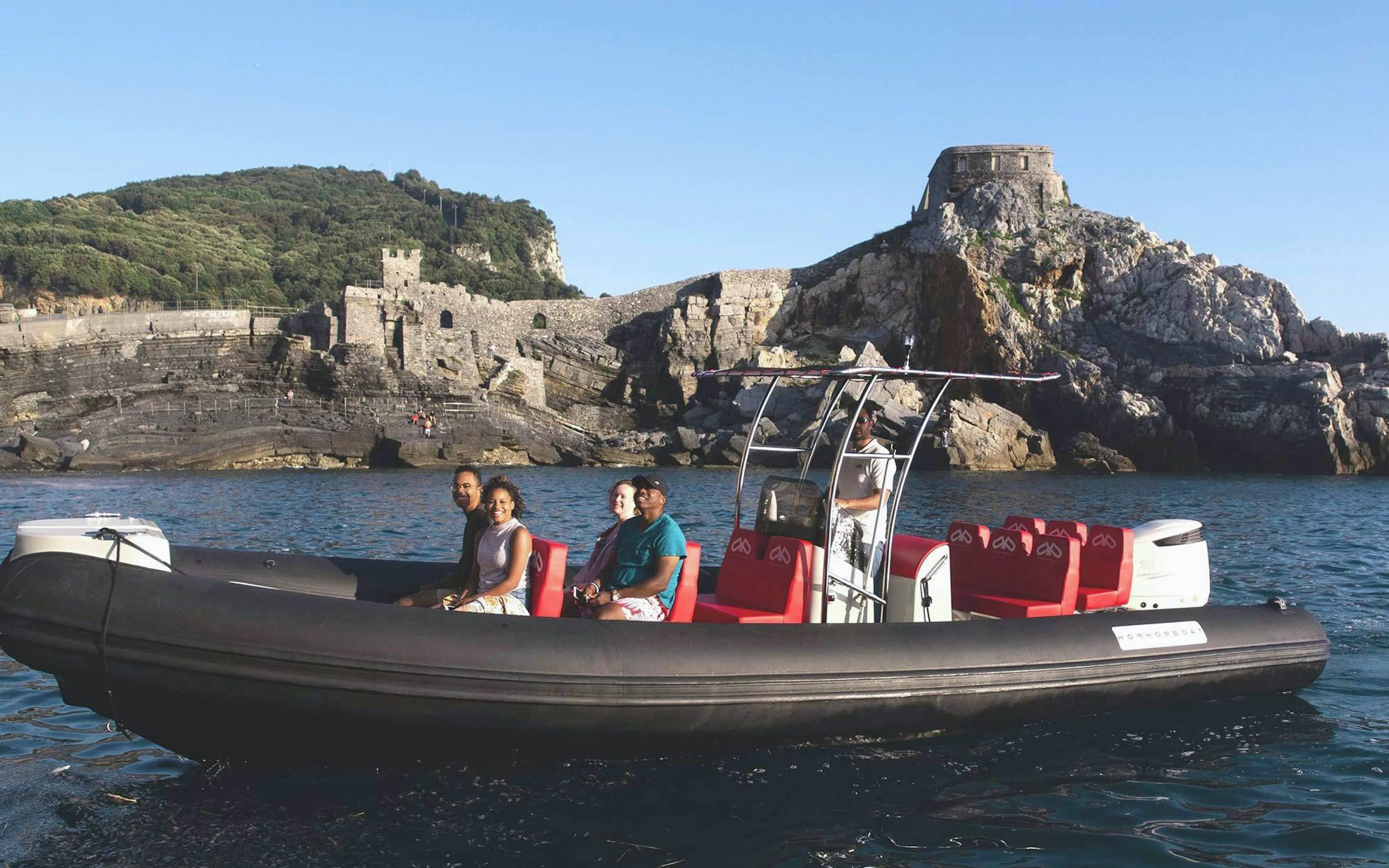 Boat with tourists near Portovenere's rocky coastline, La Spezia.