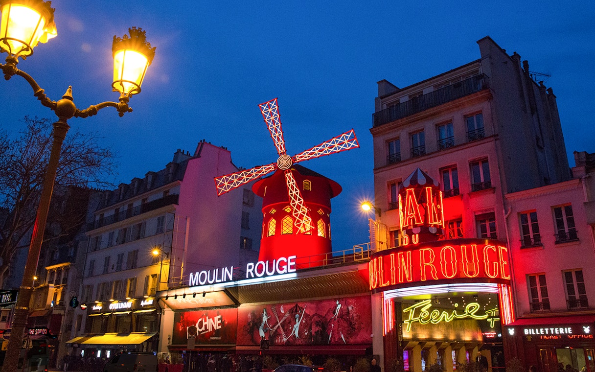 Moulin Rouge in Paris with illuminated windmill and neon signs at night.